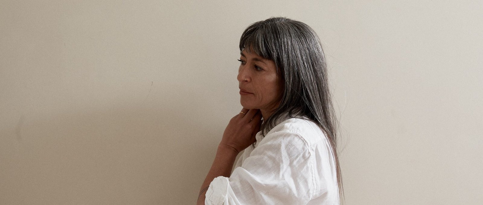 Dr Miriam A in profile, wearing a white linen shirt against a warm neutral wall